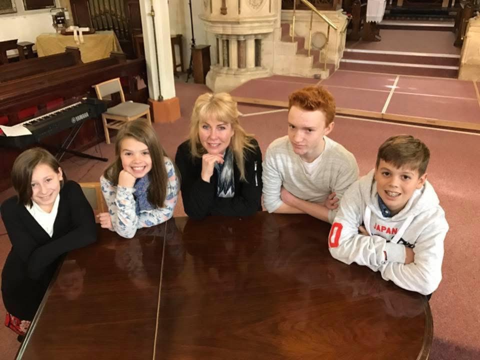 Piano teacher with four students gathered around a piano